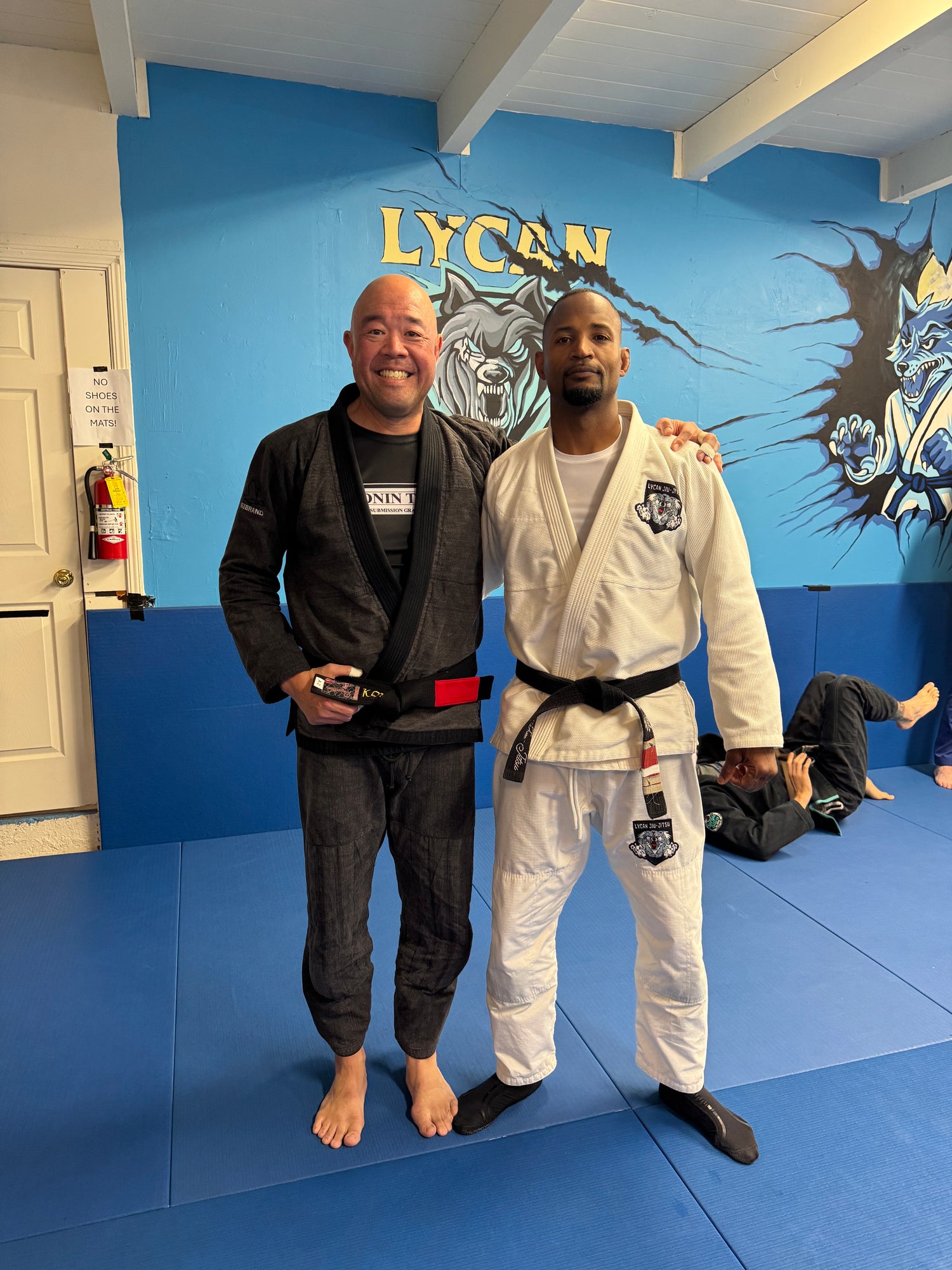 Black belt Brazilian Jiu Jitsu (BJJ) coaches in Gi standing on the mat at the Lycan Berkeley location